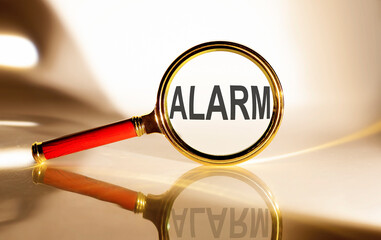 ALARM concept. Magnifier glass with text on white background in sunlight.
