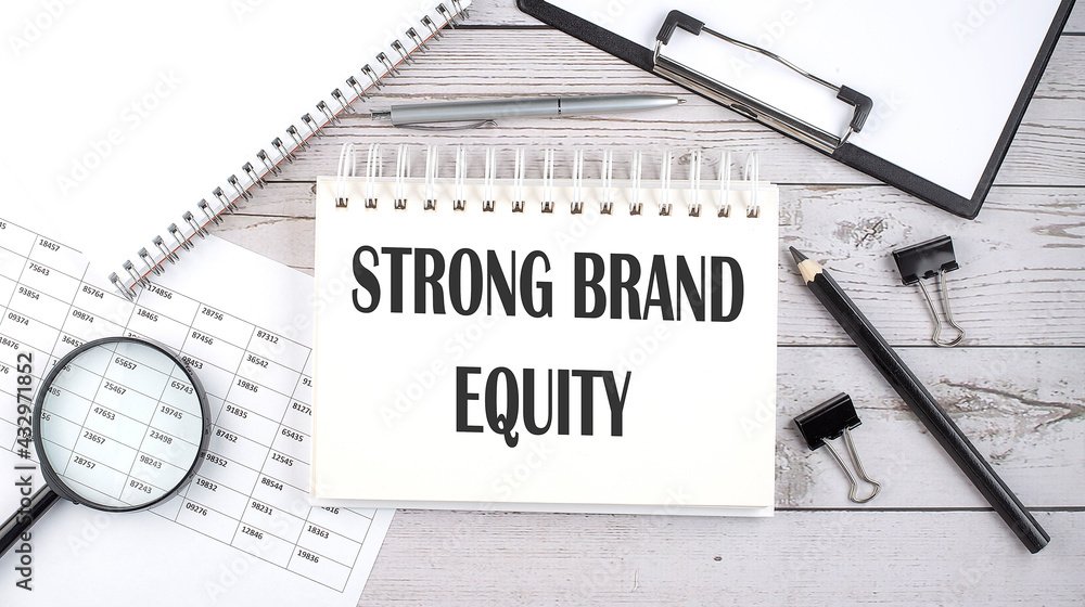 Poster notepad with text strong brand equity with a pen,office tools and graphs on the desktop.