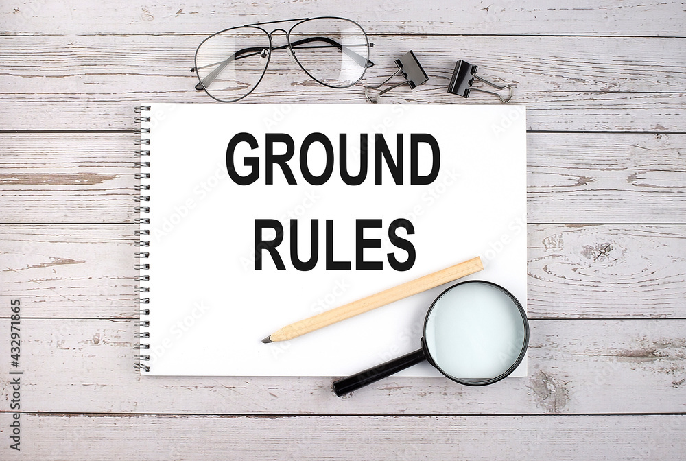 Poster notebook with text ground rules on the wooden table with pen, magnifier and glasses