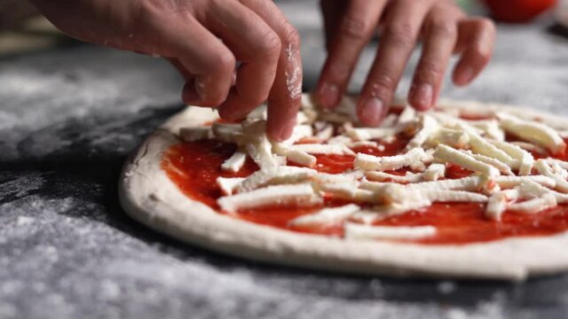 Close-up shot of a chef's hand putting the mozzarella on a fresh Napolitan Italian pizza dough for a traditional pizzaria restaurant in Italy. Napolitan food in a professional kitchen. Slow motion.