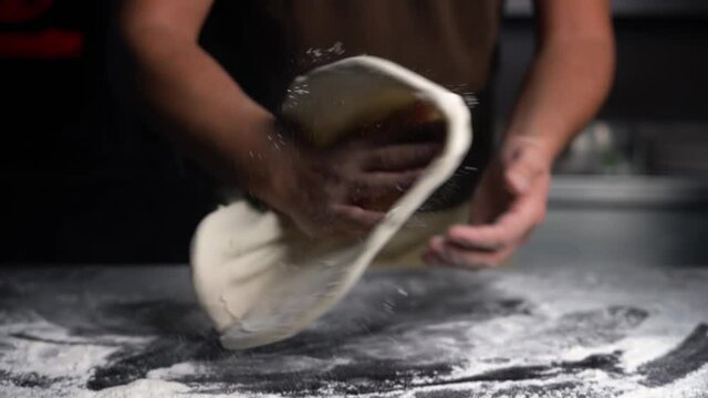 Close-up tilt-up view shot of a professional chef's hands opening a fresh Italian pizza dough for a traditional Italian pizzeria restaurant. Cooking in a Kitchen in Italy. Neapolitan food. Slow motion