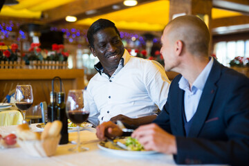 Two cheerful male friends smiling at dinner in a fashionable restaurant