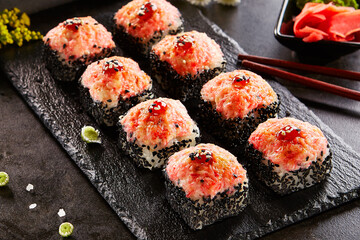 International maki sushi roll on black slate plate. Served with wooden chopstick, green wasabi and pickled ginger. Japanese set with maki sushi roll on dark stone background..