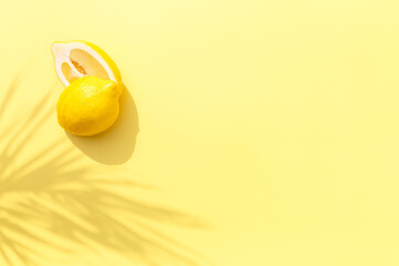 Two halved cuts of lemon with shadow from palm leaf on yellow background