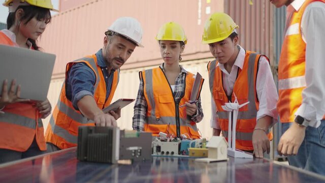 Team of engineer discuss and training solar cell system and wind turbine to new worker at warehouse cargo for export to international.Concept of container ship in import and export business logistic.