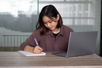 Young asian woman sitting at table doing assignments in college library.