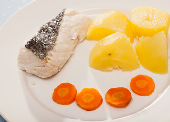 Steamed hake fillet served on white plate with boiled potatoes and carrot. Concept of diet food