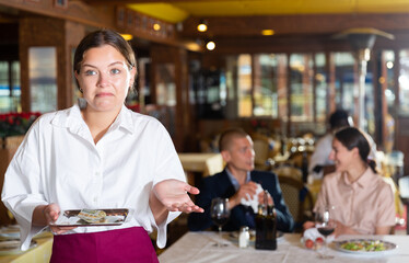 Portrait of upset waitress disappointed in small tip from guests at restaurant