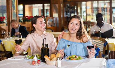 Two cheerful women friends enjoying evening meal in restaurant