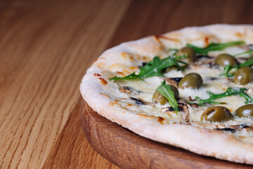Appetizing Pizza on a wooden table in a restaurant. Close-up of melted cheese, olives, mushrooms, and herbs. Freshly cooked cheese pizza on a wooden board. Italian cuisine.