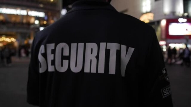 Tracking shot of a security guard walking through a street of a big city at night