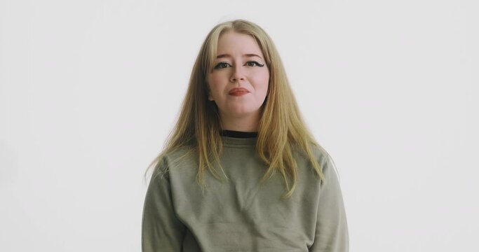 Cheerful blonde lady in green sweatshirt flirts looking into camera on white background at audition close view slow motion