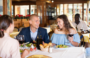 Positive friendly company eating delishious food and drinking wine in restaurant