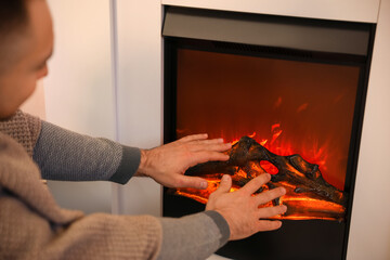 Handsome man warming hands near fireplace at home
