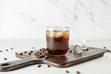 Board with glass of cold brew and coffee beans on light background