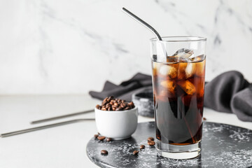 Board with glass of cold brew and coffee beans on light background