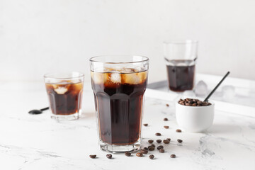 Glasses of tasty cold brew and coffee beans on light background