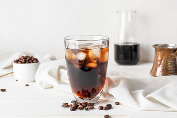 Glass of tasty cold brew and coffee beans on white background