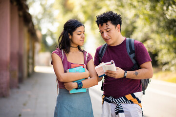 Two young students standing on street with books and talking.  Reading book.