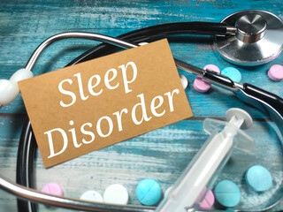 Text SLEEP DISORDER on a wooden blue background near a stethoscope, syringe and pills. Medical concept.