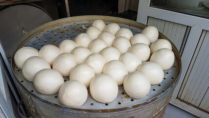Fresh steamed buns in Chinese style being prepared on a big metal steamer, The buns are all perfectly rounded. Traditional Chinese breakfast.