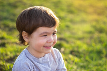 Close-up portrait. Little kid outdoors smiling and looking to the side against green grass background