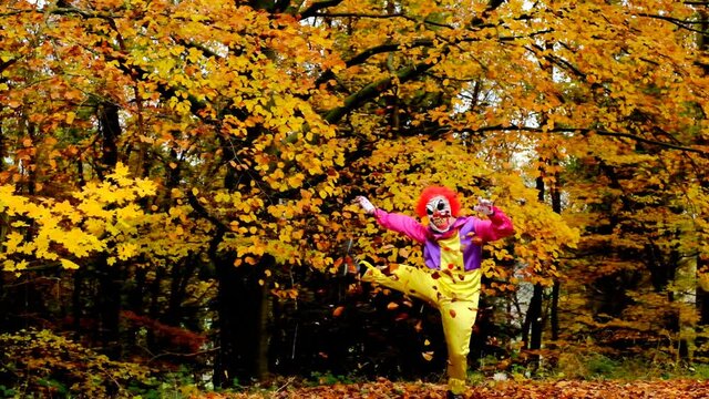 Halloween. Creepy clown throws up autumn leaves and dances in the autumn park. Halloween party.