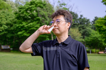 Middle-aged Asian man using nasal spray outdoors.