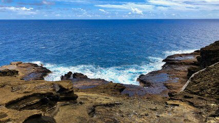 Rocky cliffs and Pacific Ocean wake surf along shoreline of coast of Hawaiian Island of Oahu,...