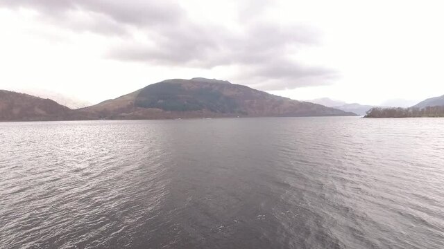 Water and mountains in autumn colors next to loch Lomond in Scotland. Drone dolly shot