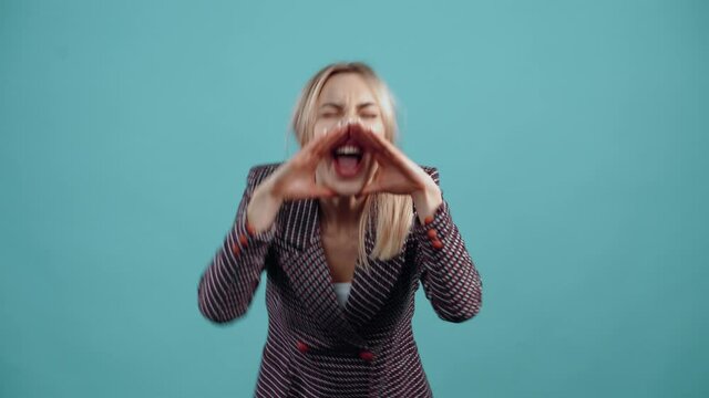The energetic blonde puts her hands to her mouth and shouts loudly at someone, she frowns confused that she hasn't been heard. Isolated on a turquoise background.The concept of life. People's emotions