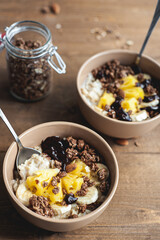 Oatmeal with pineapple, banana and chocolate granola in beige plates on a brown wooden table. A hearty healthy breakfast. A place for text.