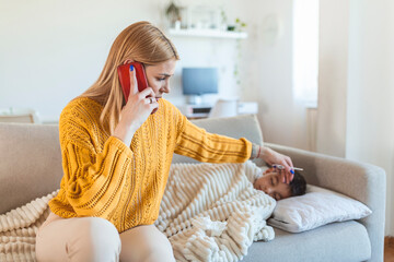 Sick boy with thermometer laying in bed and mother hand taking temperature. Mother checking temperature of her sick son and calling a doctor. Sick child with fever and illness in bed.