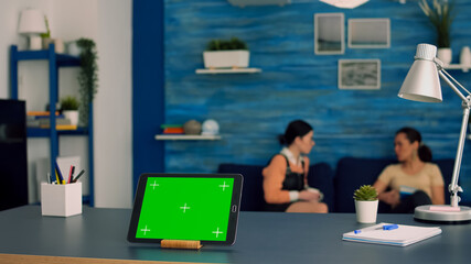 Tablet computer with mock up green screen chroma key display standing in front on office desk. Two...