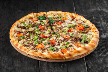 Pizza with minced meat and tomatoes on the dark wooden background