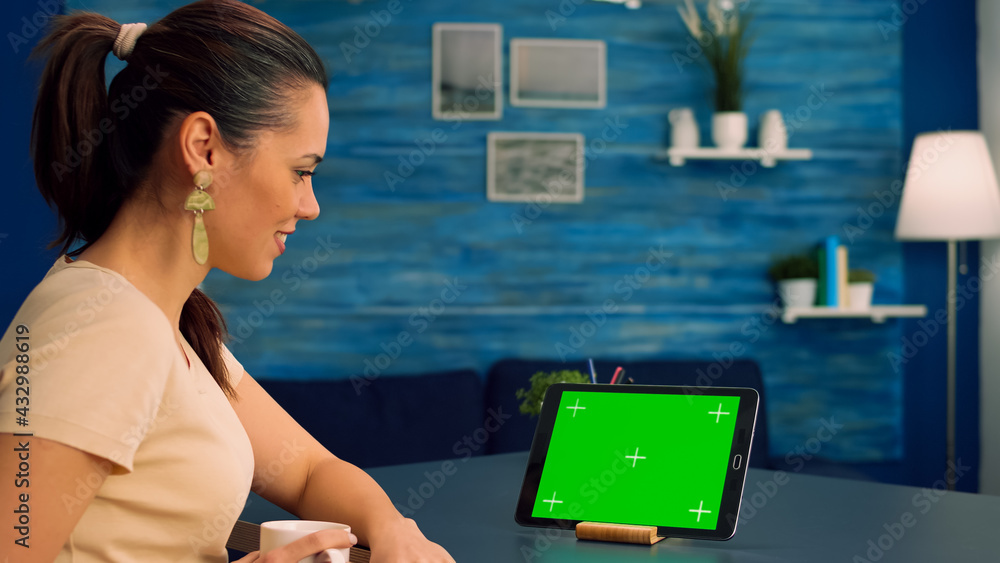 Poster freelancer holding touchpad with mock up green screen standing on office desk in living room. woman 