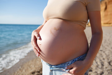 Fototapeta na wymiar heart of sand on the belly of a pregnant woman against the background of the sea