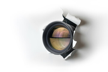 Concept of paparazzi or hidden camera, camera lens looks out through a hole in white paper wall