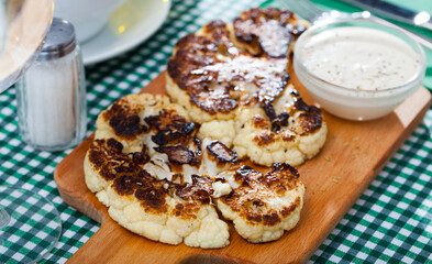 Vegetarian concept. Broiled cauliflower served on wooden board with sauce. High quality photo