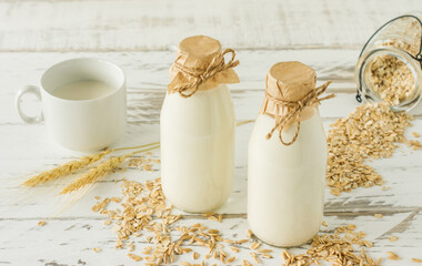 Oat milk in glass bottles and oatmeal in a cup on a wooden table.