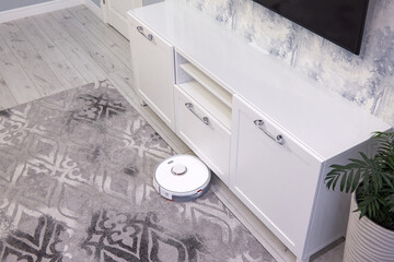 The white robot vacuum cleaner performs automatic cleaning of the gray carpet. Smart Home technology