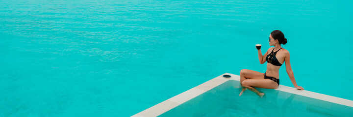 Luxury lifestyle elegant bikini woman drinking coffee cup by infinity swimming pool at overwater...