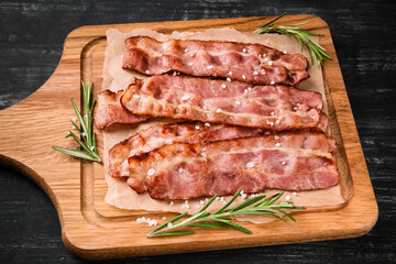 Hot fried bacon with rosemary on a black background.