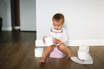 Funny kid Toddler sits on a pot with toilet paper, concept of teaching pot, child autonomy. Baby on...