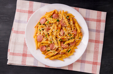 Penne pasta in tomato sauce with sausages and cheese, decorated with parsley on a  black background