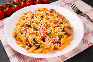 Penne pasta in tomato sauce with sausages and cheese, decorated with parsley on a  black background