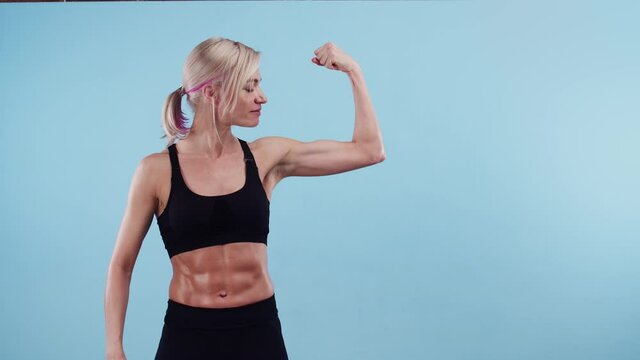 Muscular woman touches bicep with hand and smiles in the studio. Concept of sports.