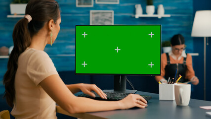 Woman looking at computer with green screen mock up chroma key display working at business...