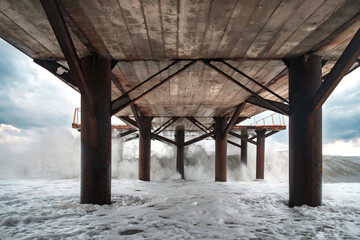 Large waves breaking on the poles of the pier, view from under the pier