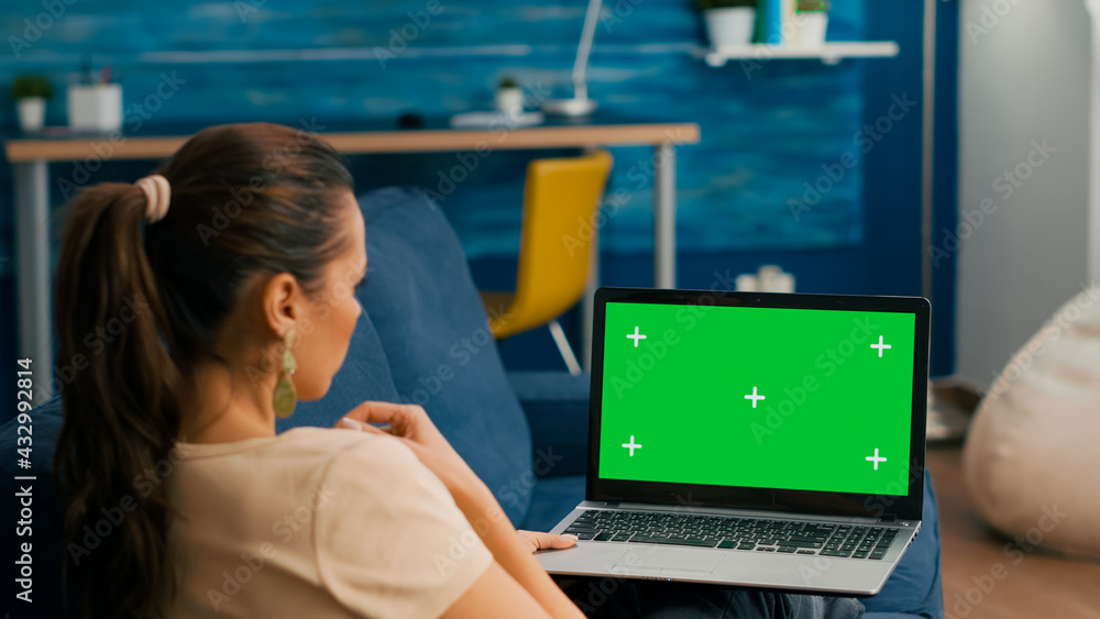 Poster freelancer sitting on couch working on business ideas using laptop computer with mock up green scree